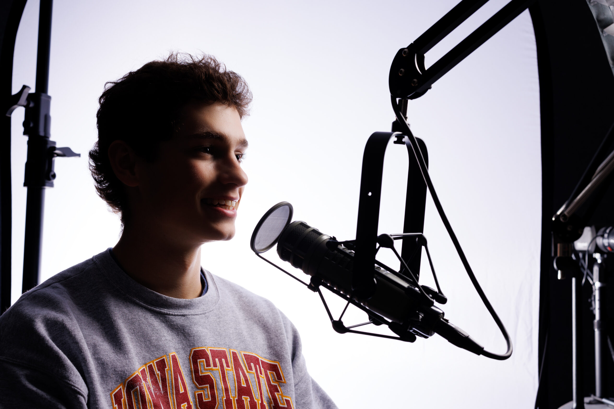 Male student wearing a grey Iowa State sweatshirt talking into a podcast mic.