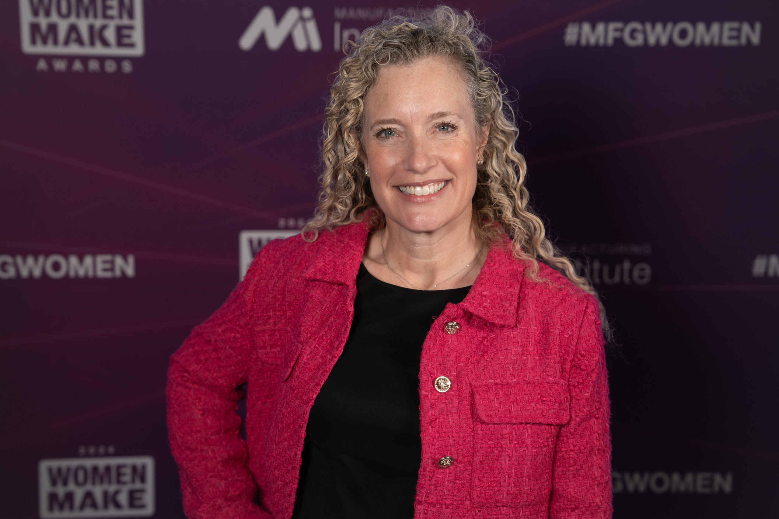 Melissa Boom stands smiling at the camera with the conference backdrop behind her.