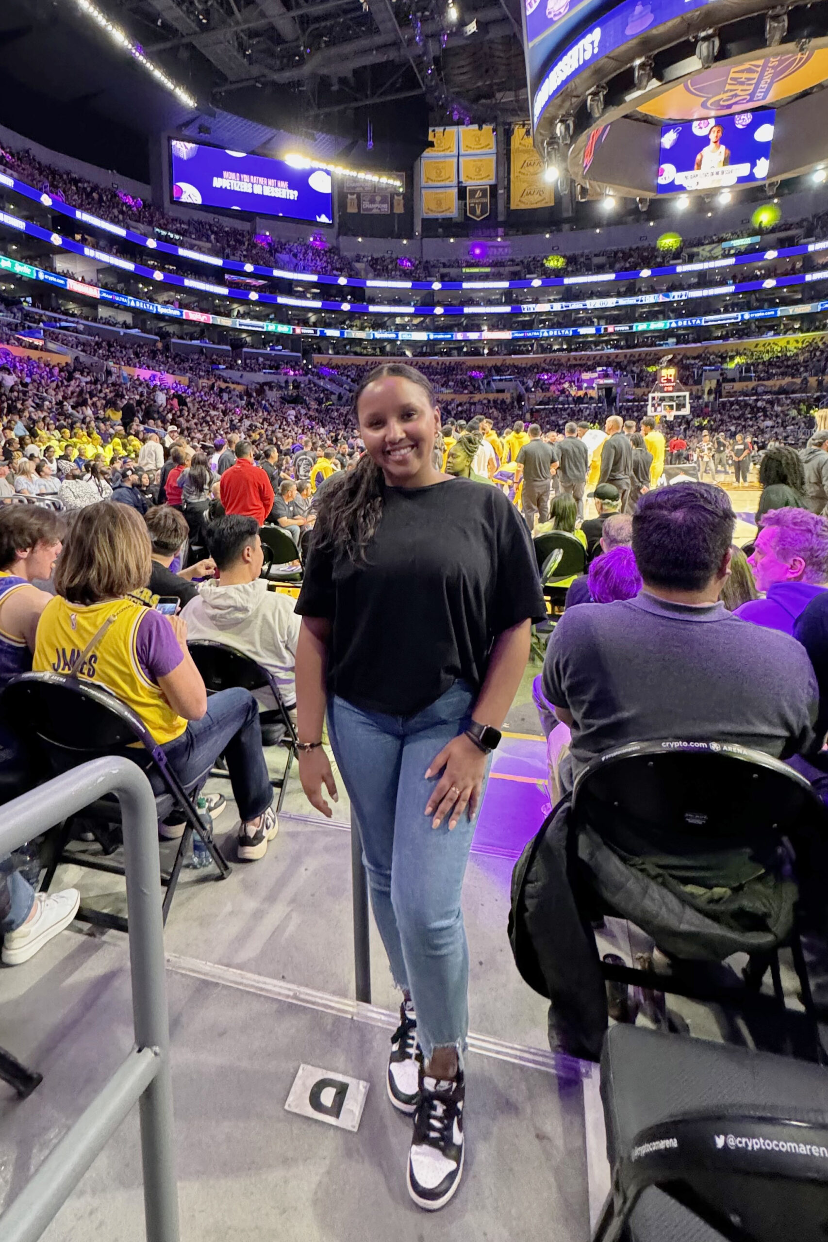 Macie VanNurdent stands smiling at camera courtside with the LA Lakers basketball court behind her.